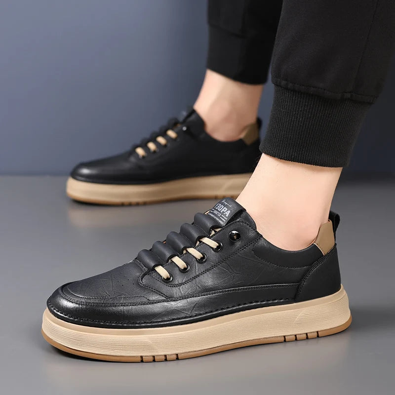 Black leather sneakers with beige soles worn by a person on a gray background