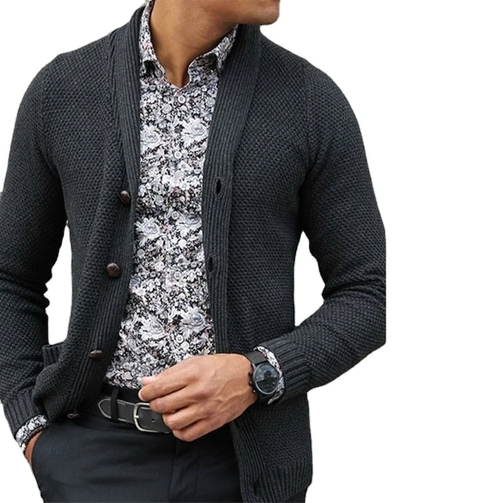 Man wearing a dark gray cardigan over a patterned shirt on a white background