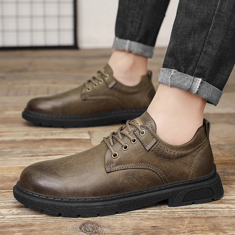 Brown leather shoes worn with rolled-up jeans on a wooden floor.