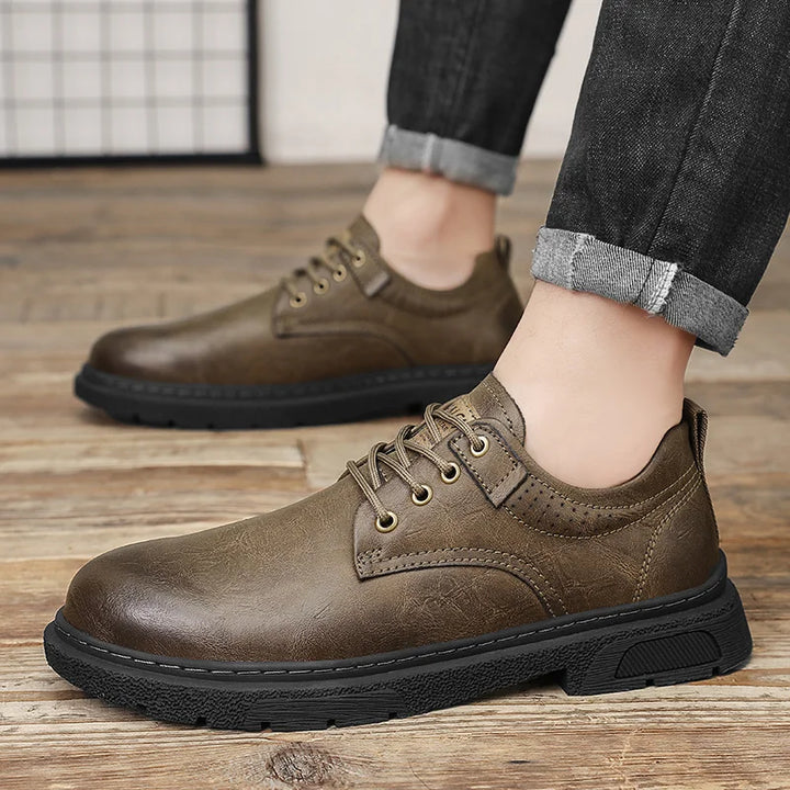 Brown leather shoes worn with rolled-up jeans on a wooden floor.