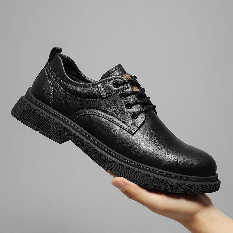 Black leather shoe held by a hand against a gray background