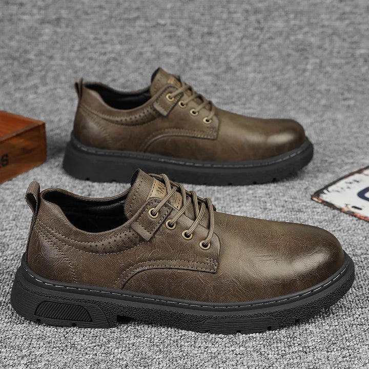 Brown leather shoes with black soles on a gray surface