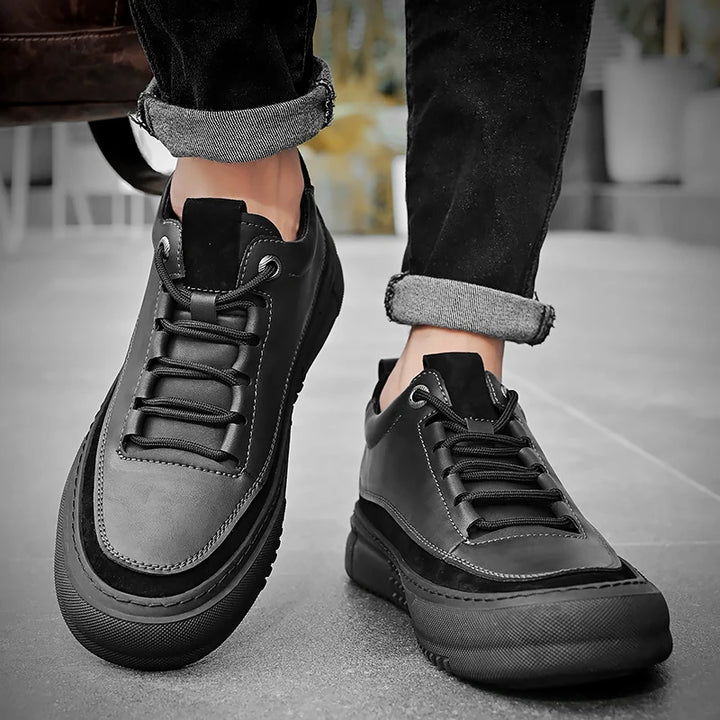 Black leather sneakers worn with rolled-up jeans on a neutral background
