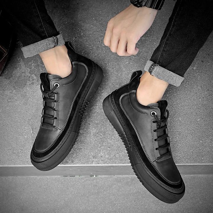 Black leather sneakers worn by a person on a gray floor.