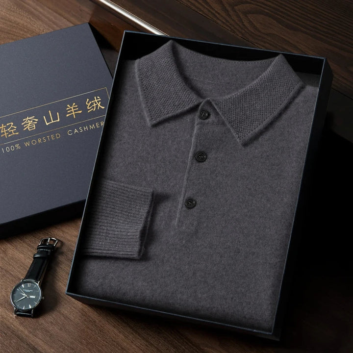 Folded gray polo shirt in a black box on a wooden surface with a watch beside it.