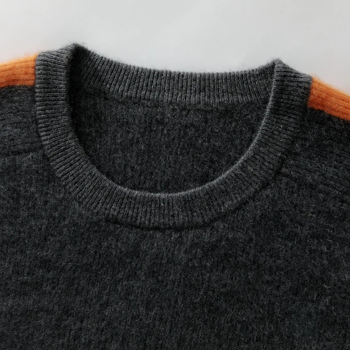 Close-up of a dark gray sweater with orange sleeves on a light gray background