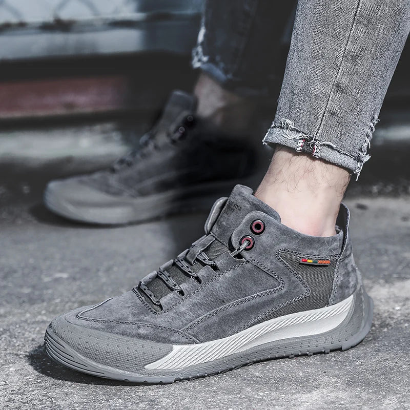 Gray suede shoes worn with rolled-up jeans on a concrete surface.