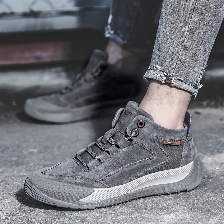 Gray suede shoes worn with rolled-up jeans on a concrete surface.