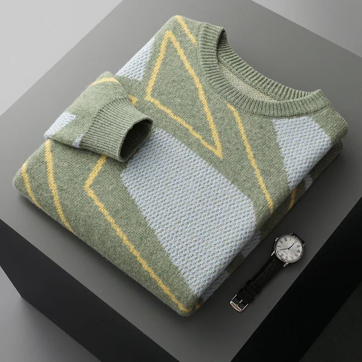 Folded green and white sweater with yellow geometric patterns on a dark surface, accompanied by a watch.
