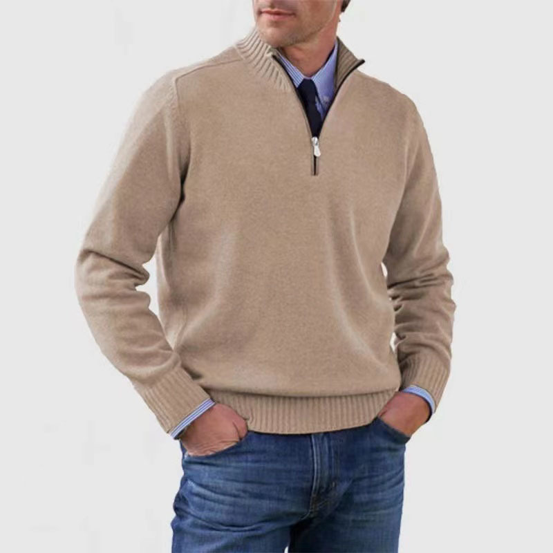 Man wearing a beige half-zip sweater with blue jeans on a light gray background