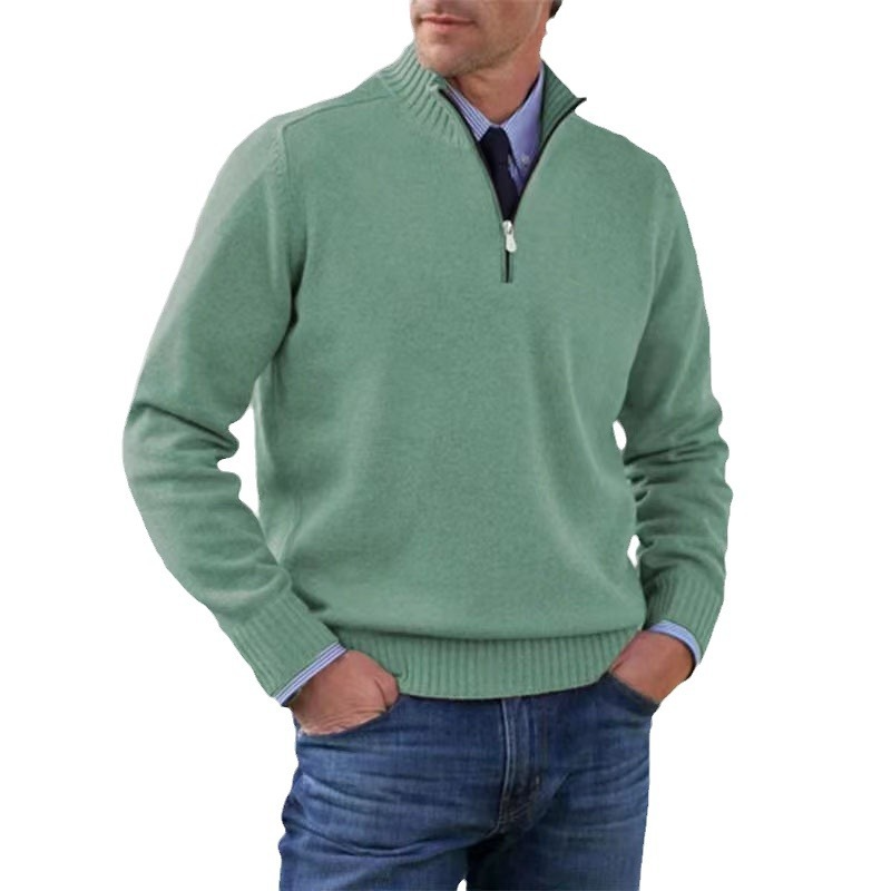 Man wearing a green sweater with a quarter zip, blue jeans, and a purple shirt underneath on a white background.