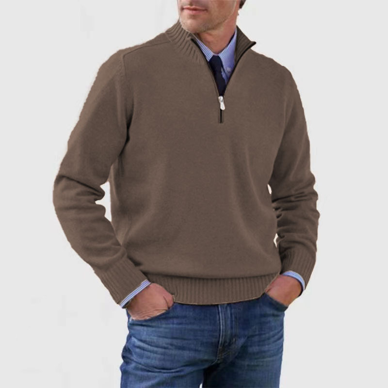 Man wearing a brown half-zip sweater over a blue shirt with jeans on a light gray background