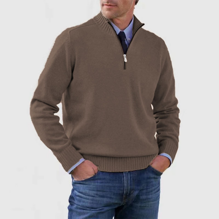 Man wearing a brown half-zip sweater over a blue shirt with jeans on a light gray background