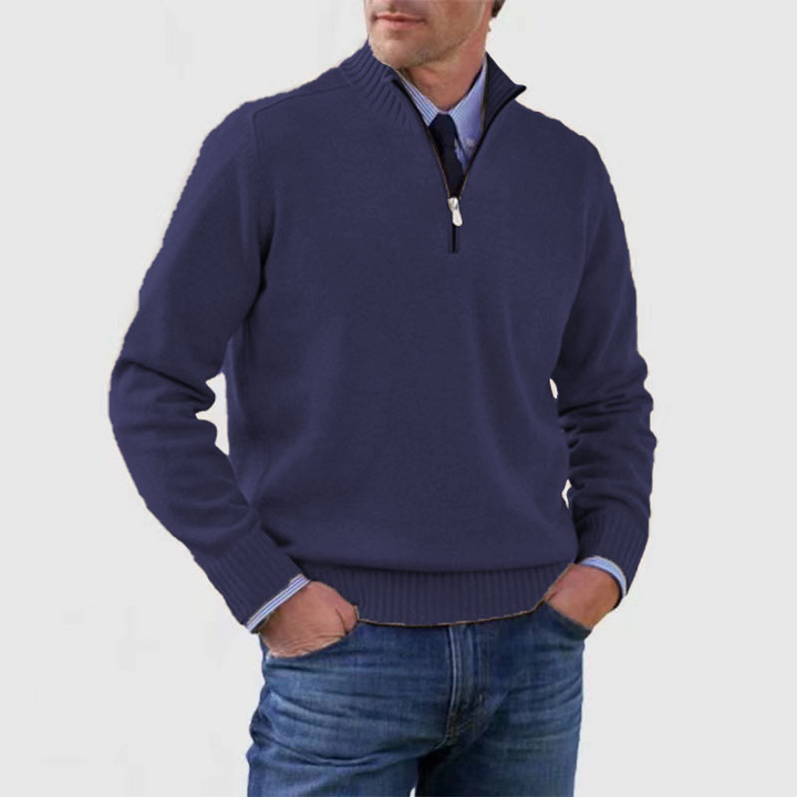 Man wearing a navy blue sweater with a zipper, light blue shirt, and jeans on a white background