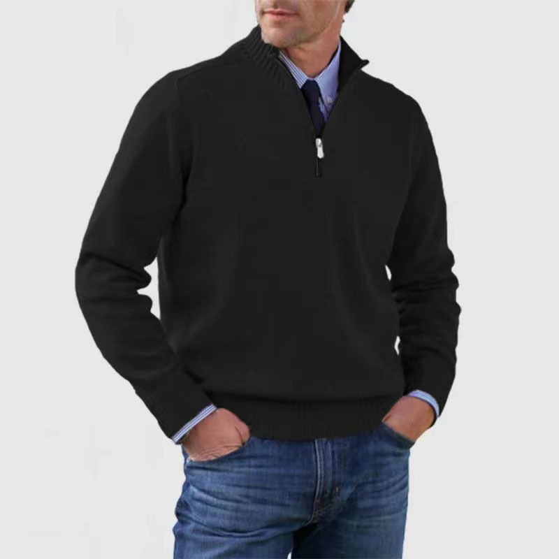 Man wearing a black quarter-zip sweater over a collared shirt with blue jeans on a light gray background