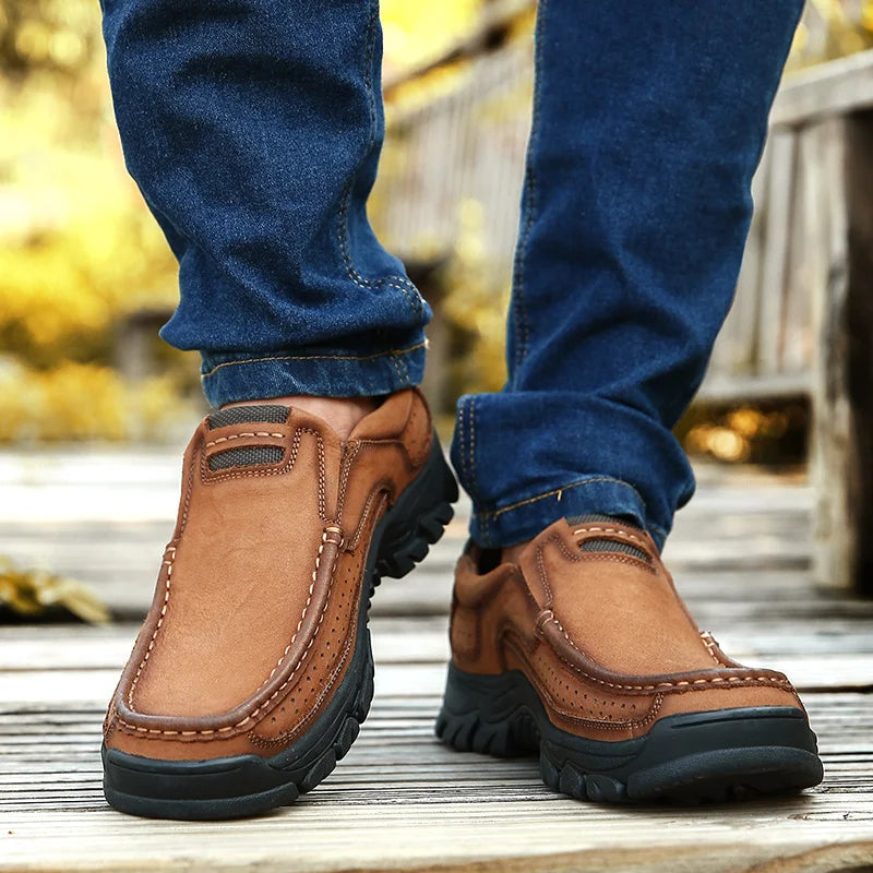 Brown leather shoes worn with blue jeans on a wooden floor.