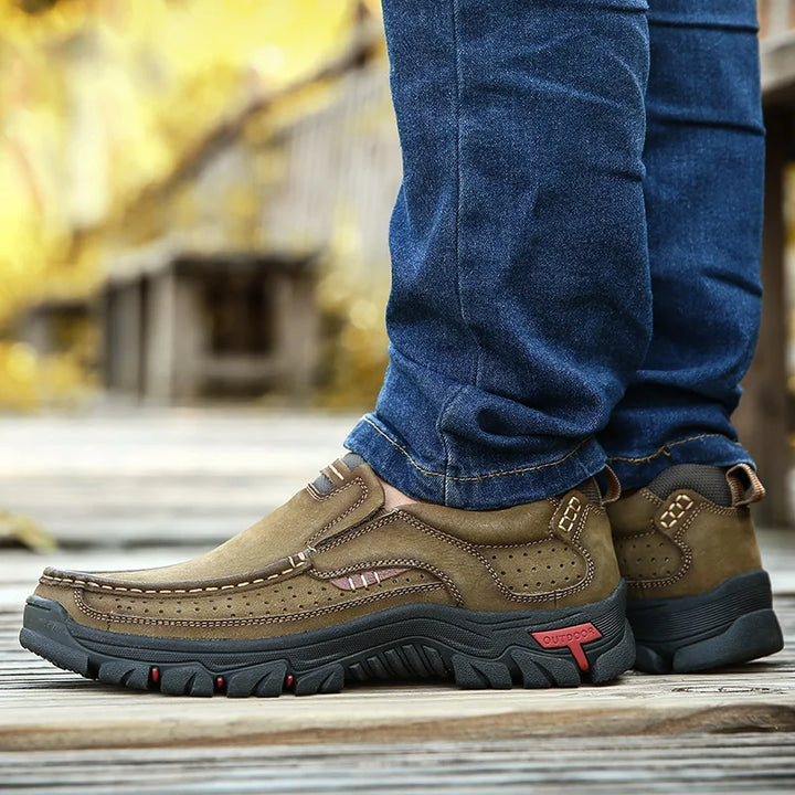 Brown shoes with black soles worn with blue jeans on a blurred outdoor background