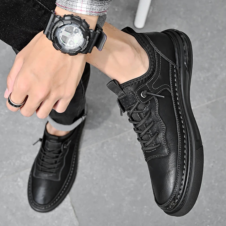 Person wearing black leather shoes and a black watch on a gray background