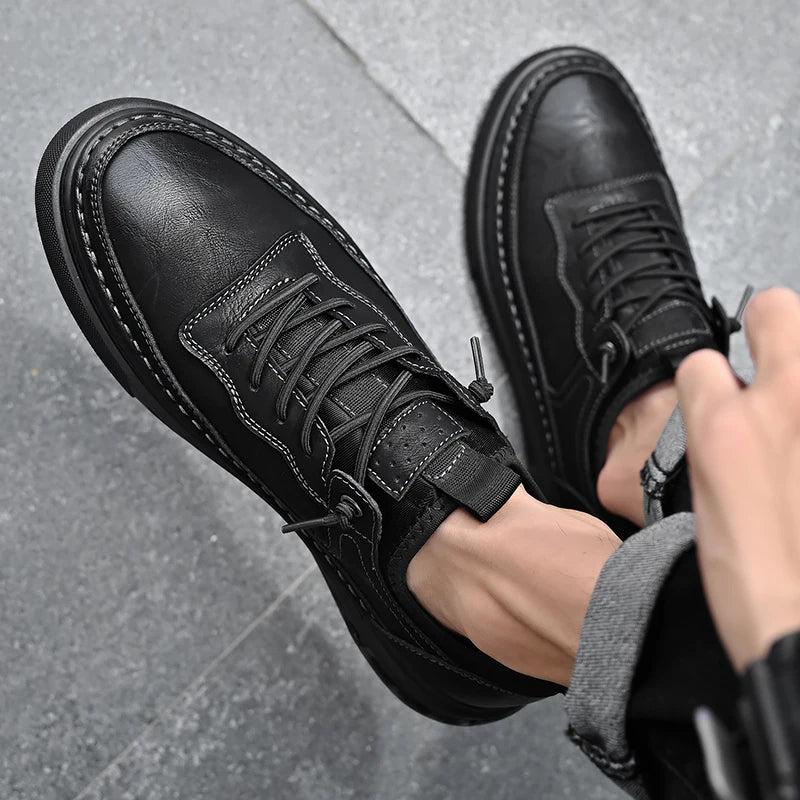 Black leather boots being worn on a gray pavement background