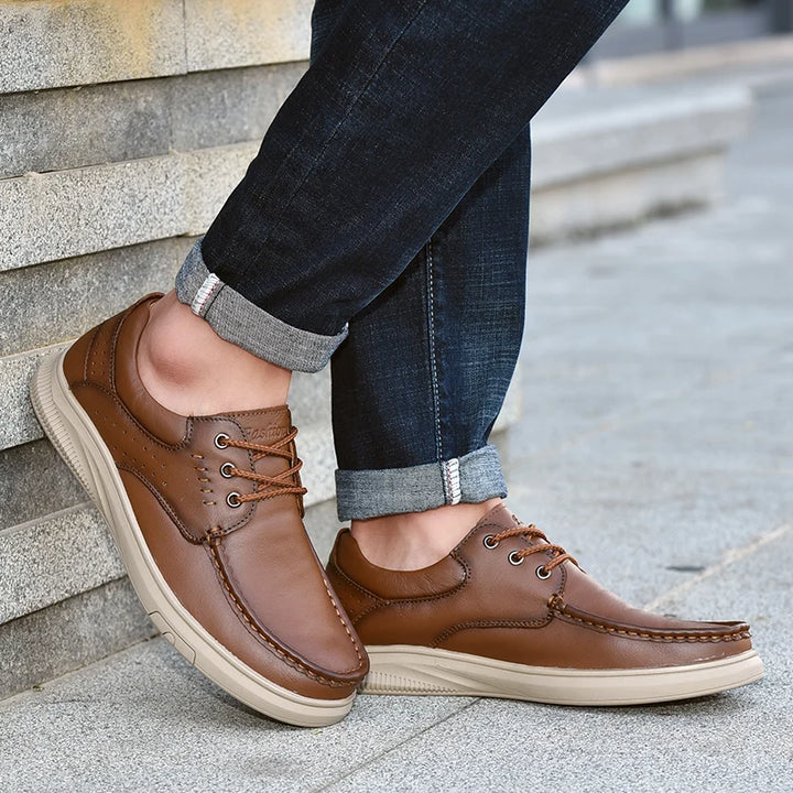 Brown leather shoes worn with rolled-up jeans on a stone step.