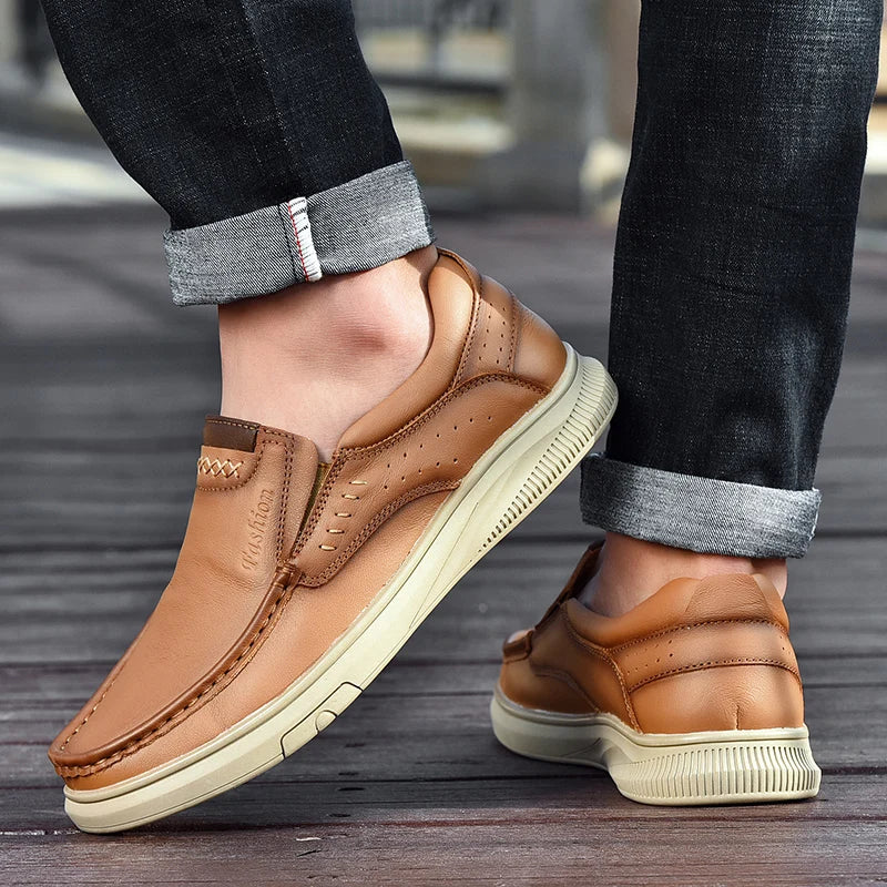 Brown leather shoes worn with rolled-up jeans on a wooden floor.