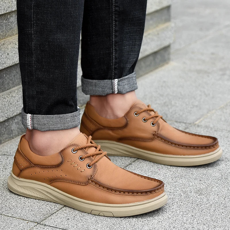 Brown leather shoes worn with dark jeans on a stone pavement.