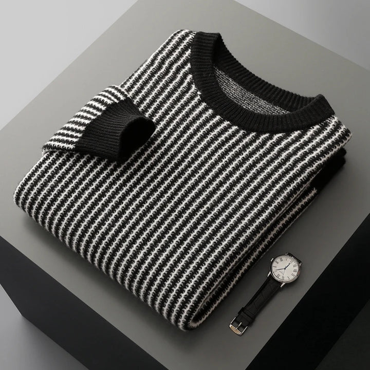 Folded black and white striped sweater with a watch on a gray surface