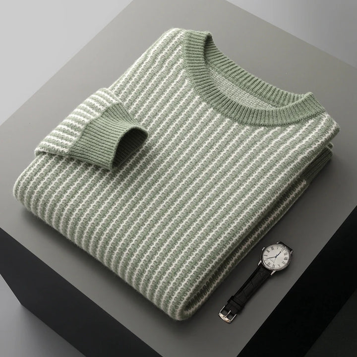 Folded green and white striped sweater on a gray surface with a watch.