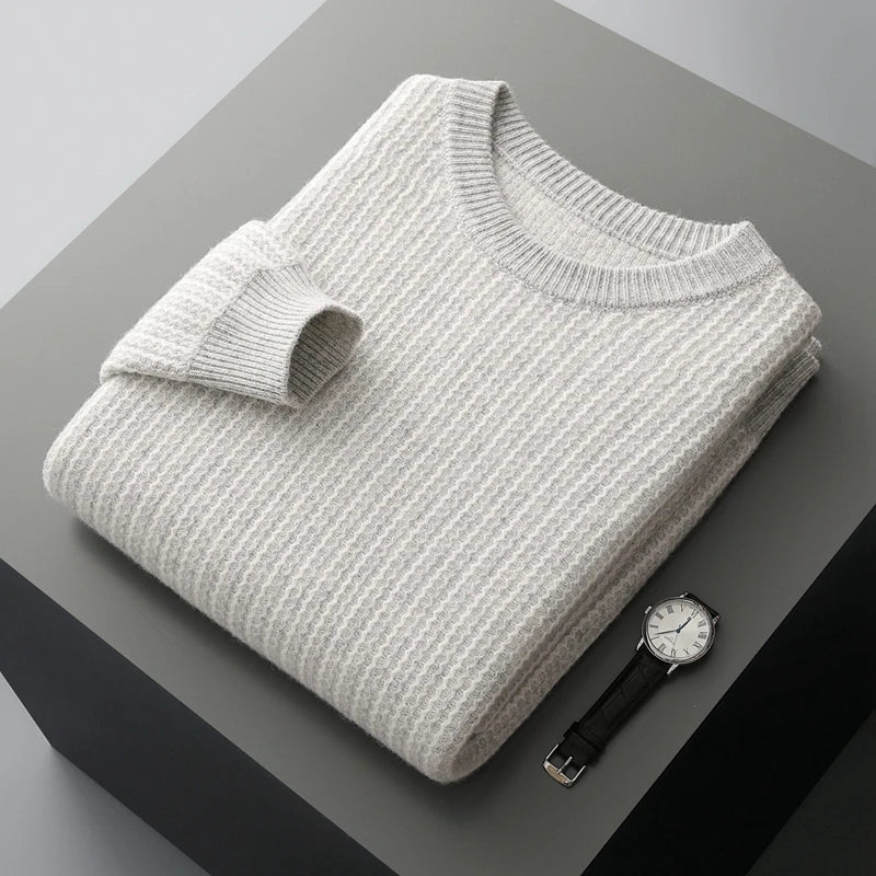 Folded gray sweater on a dark surface with a watch beside it
