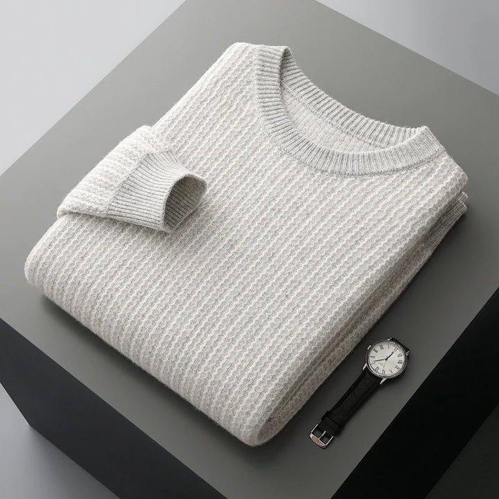 Folded gray sweater on a dark surface with a watch beside it