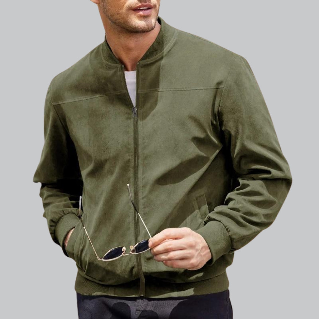 Man wearing a green bomber jacket holding sunglasses against a gray background