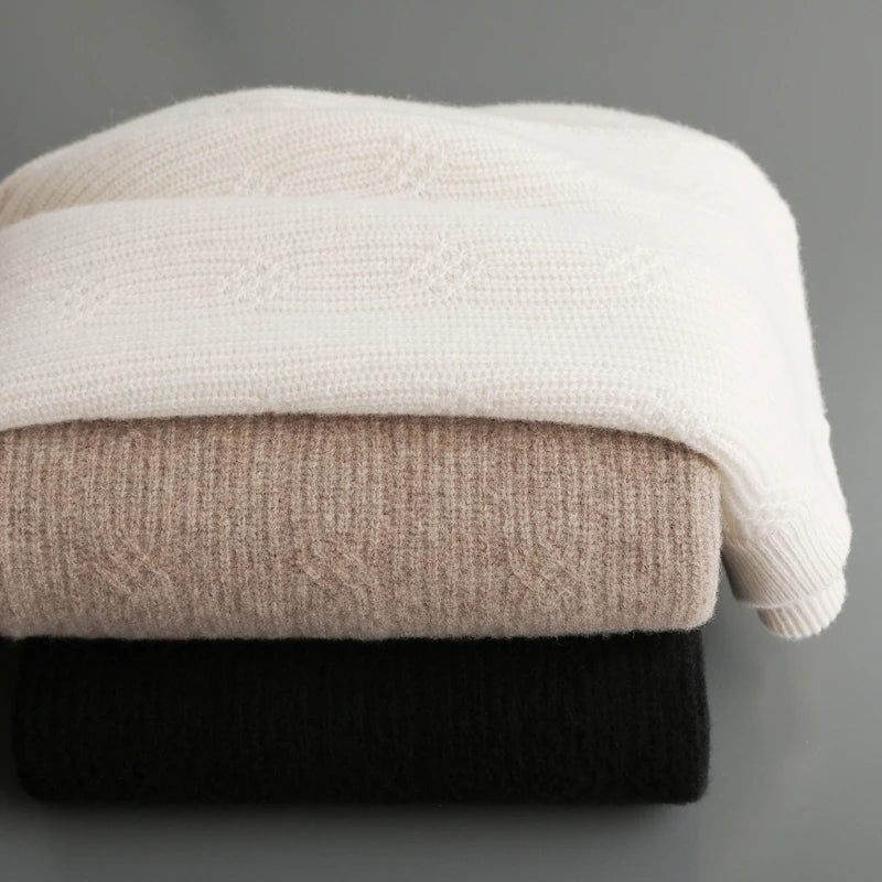 Stack of three folded sweaters in white, beige, and black on a gray background