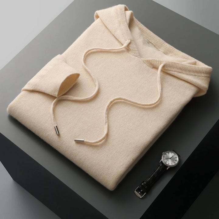 Beige hoodie folded on a dark surface with a watch beside it