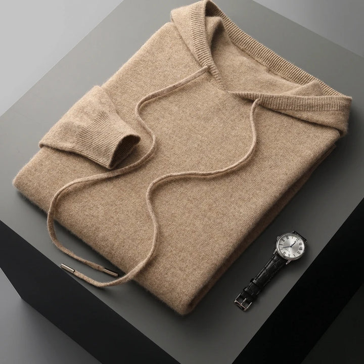 Folded beige sweater on a dark surface with a watch beside it