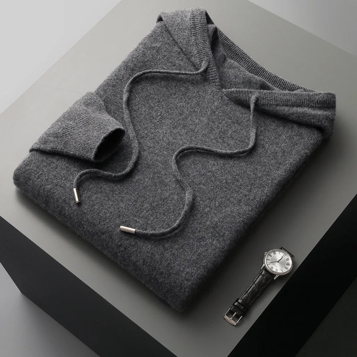 Folded gray sweater with a watch on a gray surface