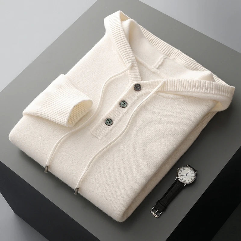 Folded cream-colored sweater with black buttons on a gray surface, accompanied by a black watch.