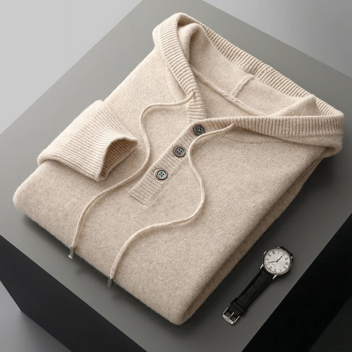 Folded beige sweater with a watch on a gray surface