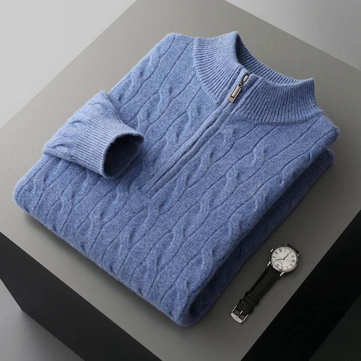 Folded blue cable knit sweater with a watch on a gray surface