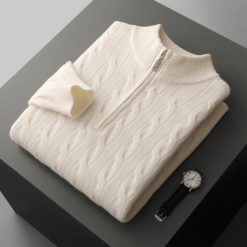 Folded cream-colored cable-knit sweater on a dark surface with a watch beside it.