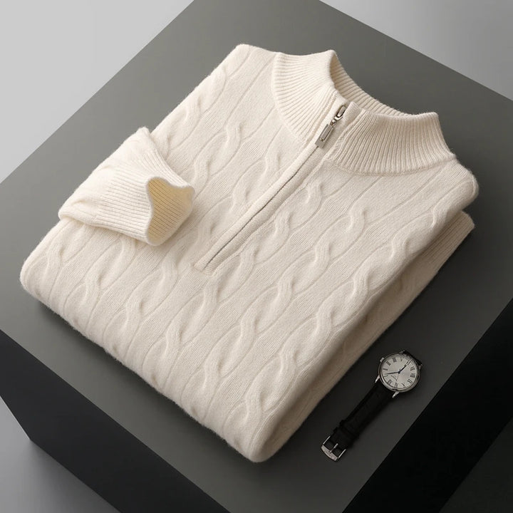 Folded cream-colored cable-knit sweater on a dark surface with a watch beside it.