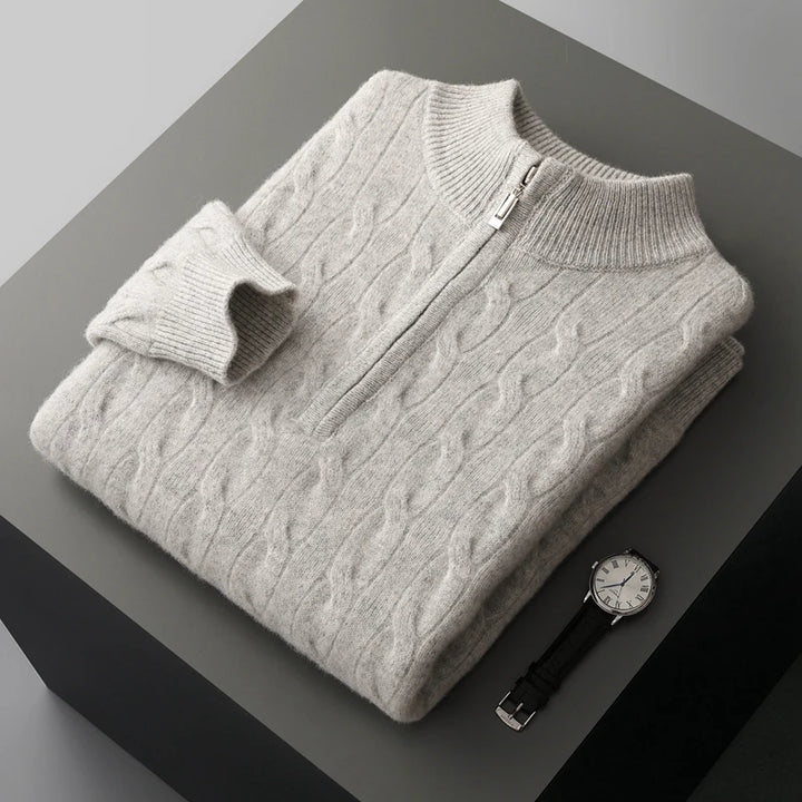 Folded gray cable knit sweater on a dark surface with a watch.