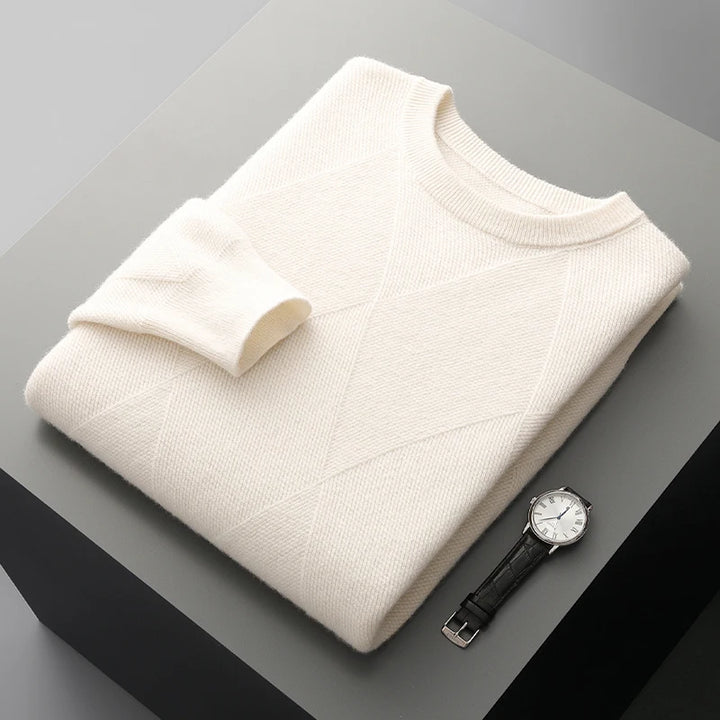 Folded cream sweater on a gray surface with a black wristwatch.