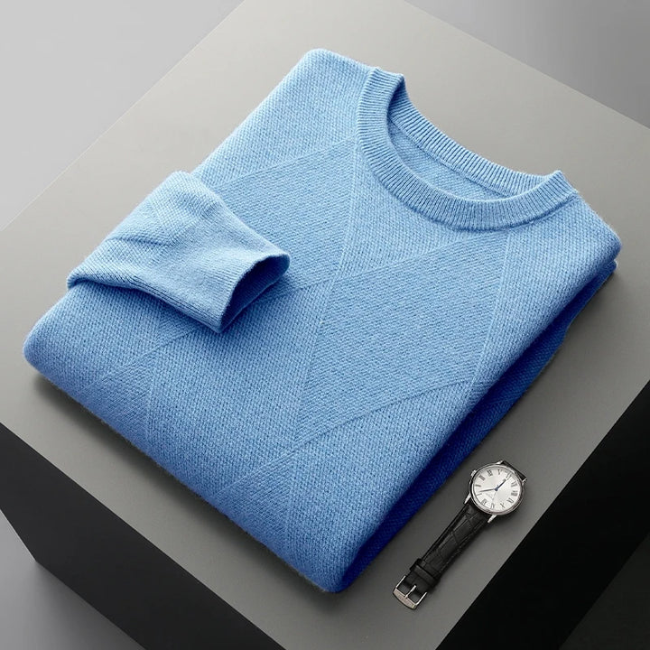 Folded blue sweater on a gray surface with a watch next to it