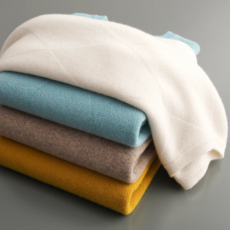 Stack of folded sweaters in white, blue, beige, and mustard yellow on a gray background