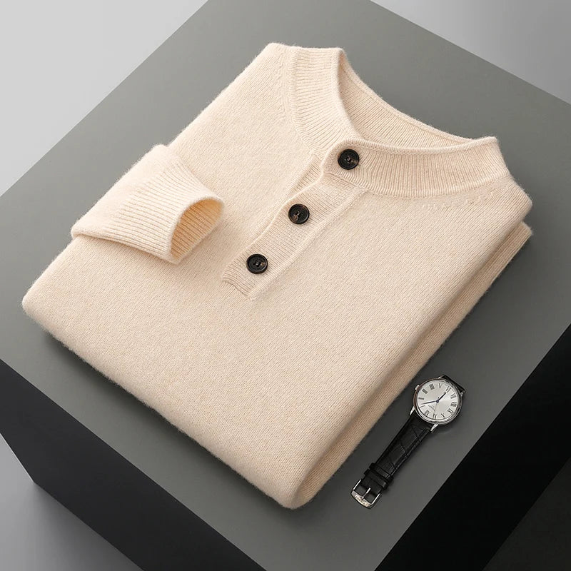 Folded beige sweater with black buttons on a gray surface, accompanied by a black watch.