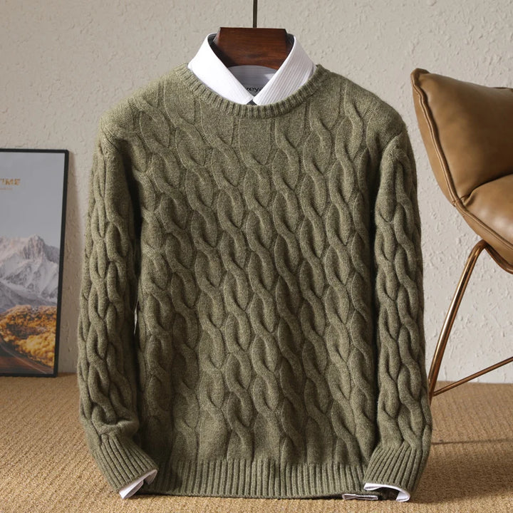Green cable knit sweater on a hanger against a neutral wall with a chair and framed picture in the background.