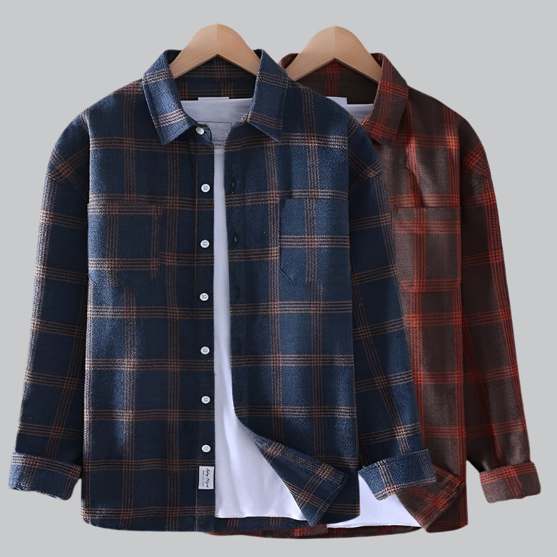 Two plaid shirts on hangers against a gray background