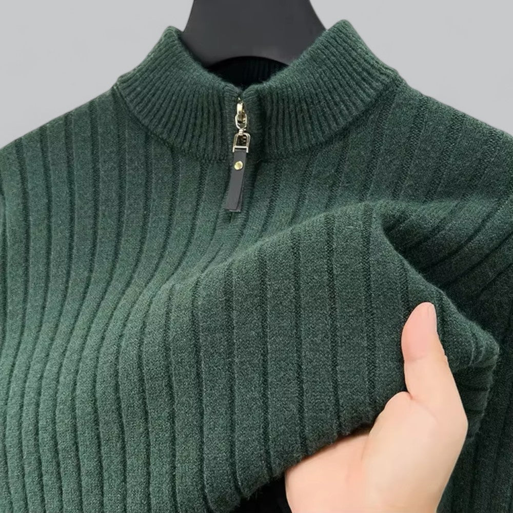 Green ribbed sweater with a zipper held by a hand against a gray background