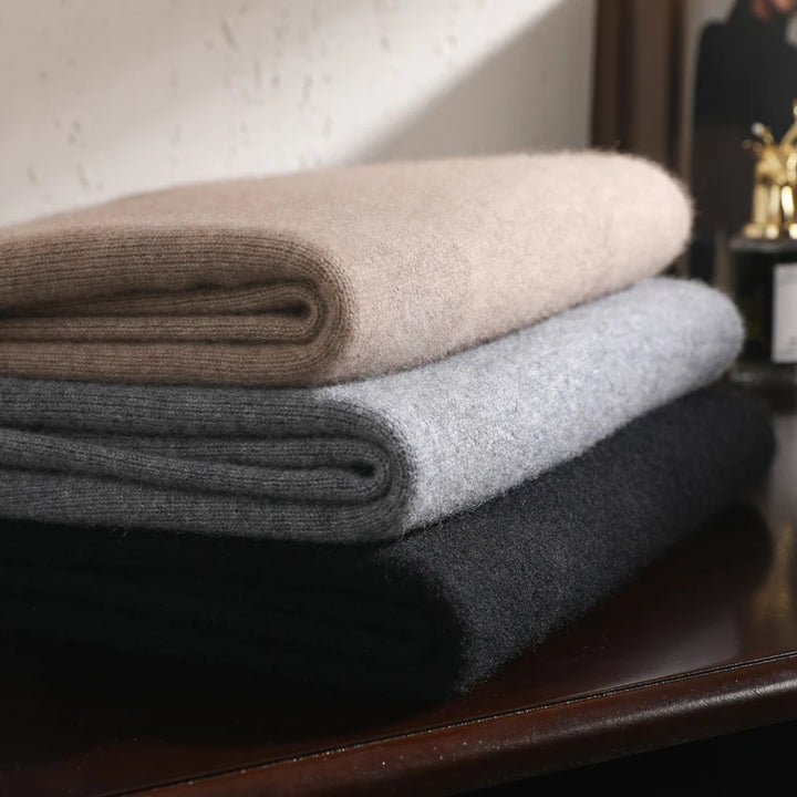 Stack of folded blankets in beige, gray, and black on a wooden surface.
