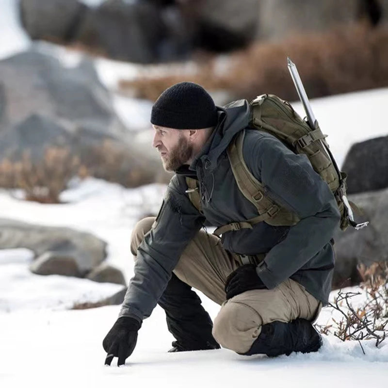 Man in winter gear crouching in a snowy landscape with a rifle.